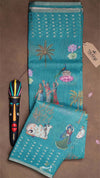 Teal fabric with embroidered designs on a brown surface, featuring a tag labeled 'Timmee'.
