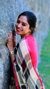 Woman in a colorful saree leaning against a stone wall with a blurred green background