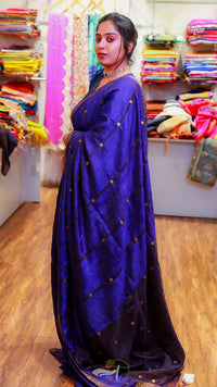 Woman wearing a blue saree with a pattern of gold dots in a fabric store.