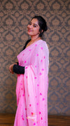 Woman wearing a pink saree with heart patterns against a patterned wall.
