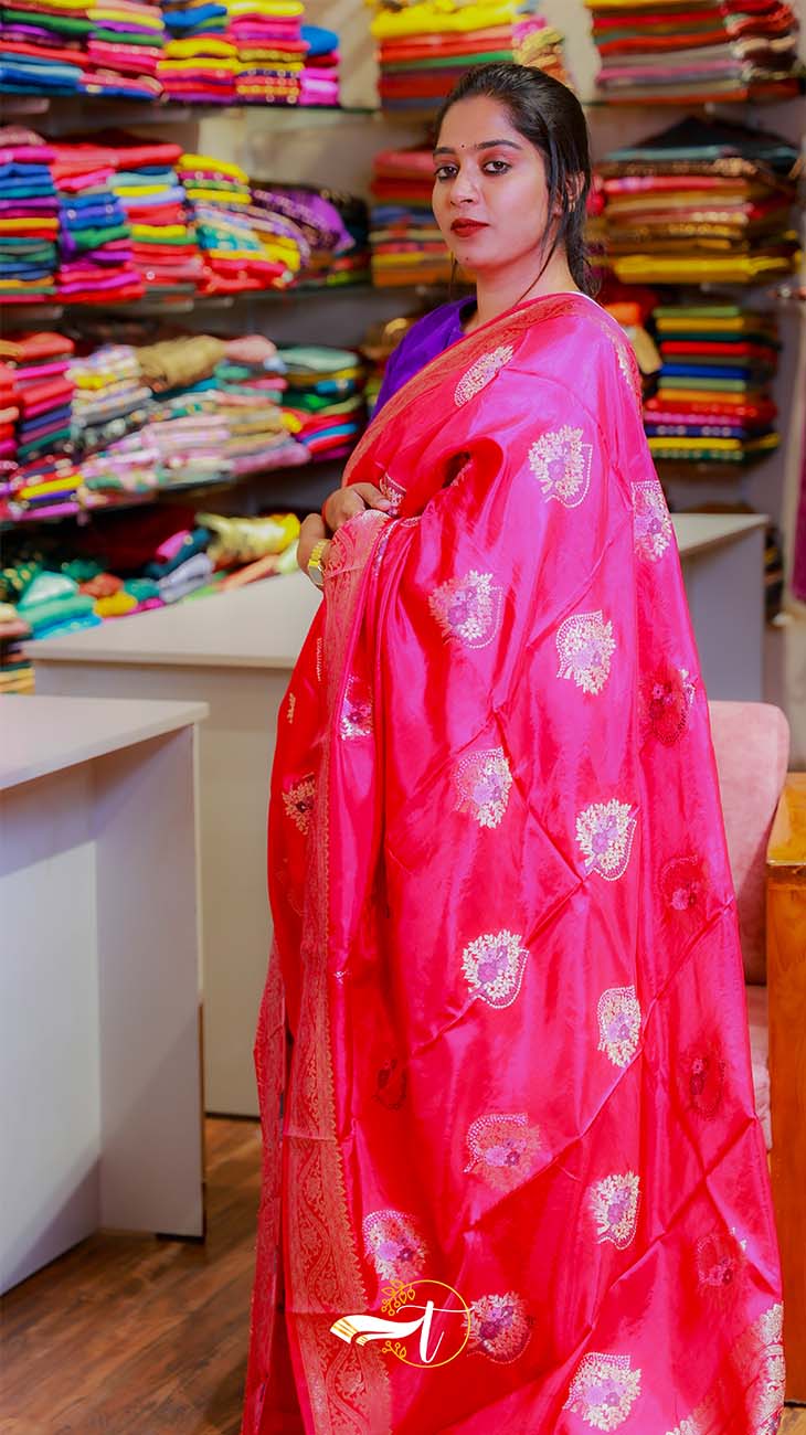 Woman in a red saree with floral patterns in a fabric store.