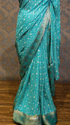Teal saree with white patterns on a wooden floor and patterned wall background