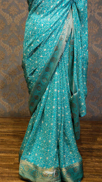 Teal saree with white patterns on a wooden floor and patterned wall background