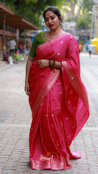 Woman wearing a pink saree with a green blouse on a street.