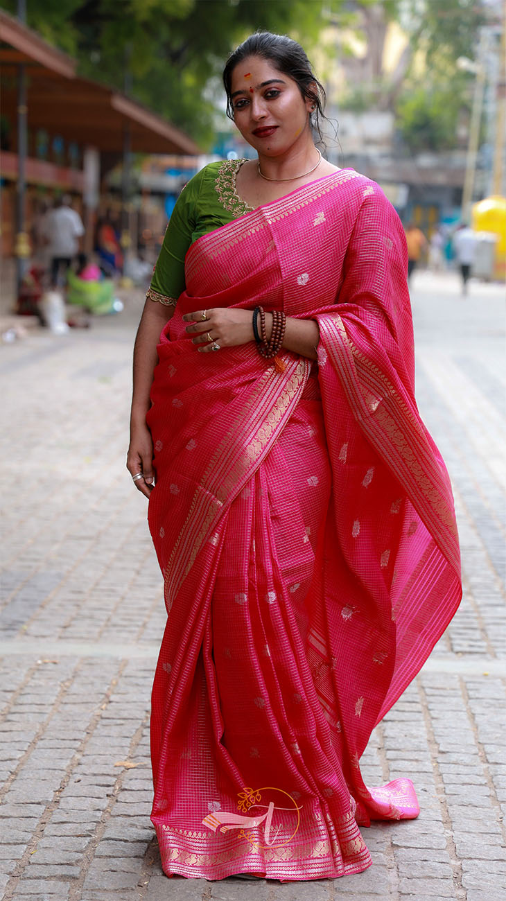 Woman wearing a pink saree with a green blouse on a street.