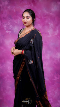 Woman in a black saree with gold border against a pink and purple gradient background
