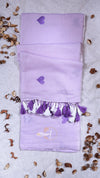 Purple scarf with heart patterns and tassels on a textured surface with small plants.