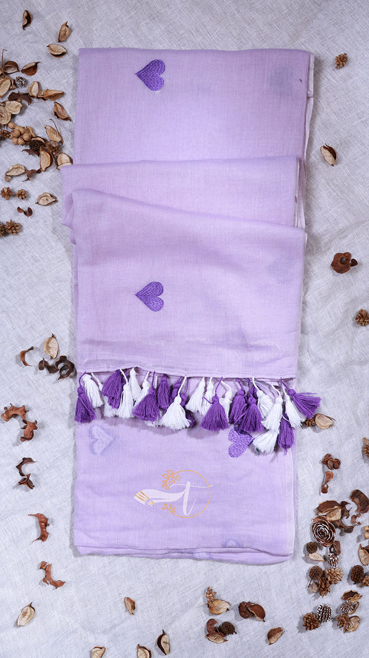 Purple scarf with heart patterns and tassels on a textured surface with small plants.