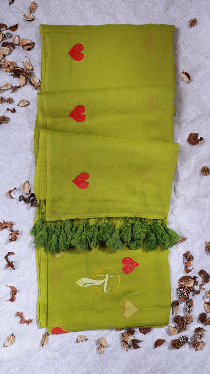 Green fabric with red heart designs and tassels on a textured surface