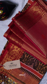 Red saree with gold patterns and a THANVI tag on a textured surface