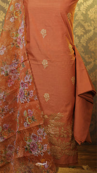 Orange fabric with floral patterns and gold embroidery against a patterned wall.