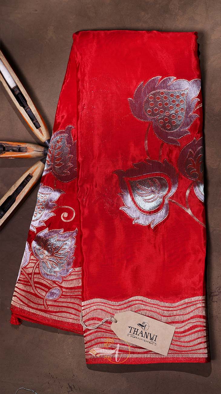 Red fabric with silver floral embroidery on a brown surface, featuring the THANU brand.