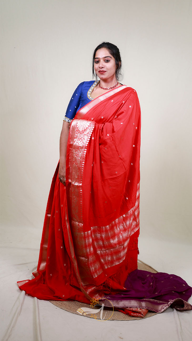 Woman wearing a red saree with a blue blouse against a plain background