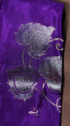 Purple fabric with silver floral embroidery on a brown background