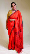 Woman wearing a bright red saree with a yellow blouse against a plain background