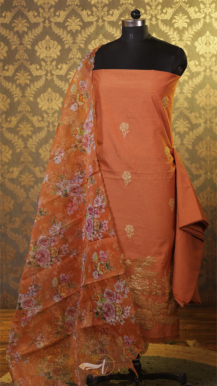 Orange saree with floral patterns on a mannequin against a patterned wall.