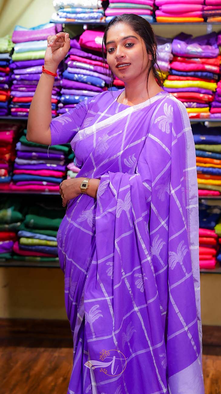 Woman wearing a purple saree with a white border in a fabric store.