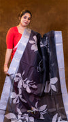 Woman holding a dark floral saree against a brown background