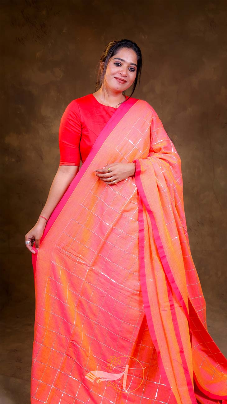 Woman wearing a bright orange saree with a red blouse against a brown background