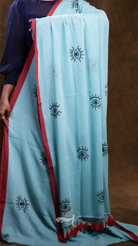 Light blue saree with eye patterns and red border held by a person against a brown background