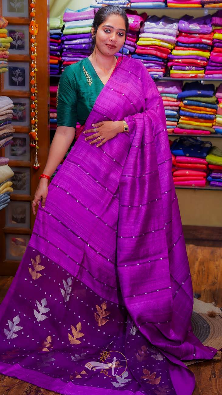 Woman wearing a purple saree with a green blouse in a fabric store.