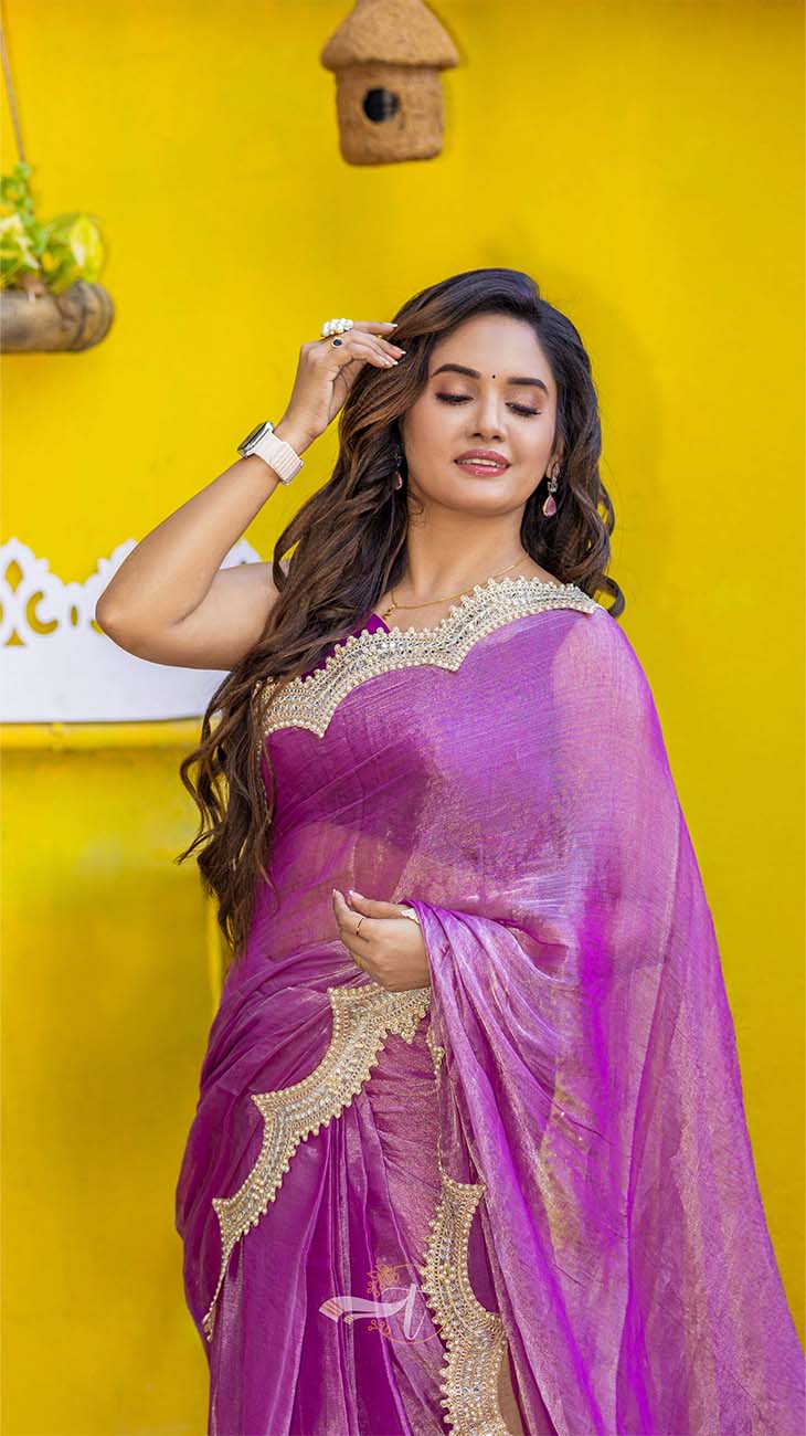 Woman in a purple saree with gold border against a yellow wall