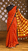 Orange saree with yellow polka dot pattern on a mannequin against a patterned wall.