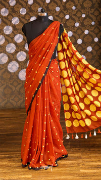 Orange saree with yellow polka dot pattern on a mannequin against a patterned wall.