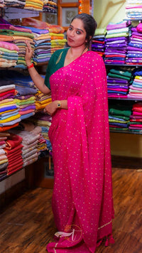 Woman in a pink saree standing in front of a display of colorful fabrics.