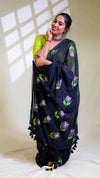 Woman wearing a black saree with purple floral patterns in a well-lit room.