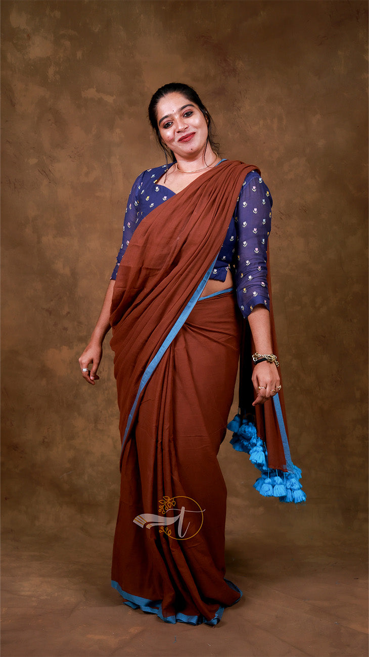 Woman wearing a brown saree with blue blouse against a brown background