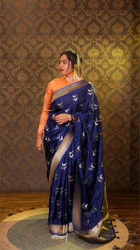 Woman wearing a blue saree with a pattern against a decorative wall.