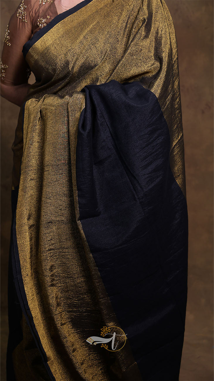 Saree with gold and navy fabric draped over a person against a brown background