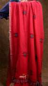 Red fabric with black embroidered designs on a brown background