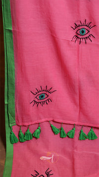 Pink fabric with embroidered eye designs and green tassels on a green background