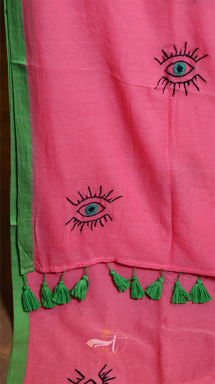 Pink fabric with embroidered eye designs and green tassels on a green background