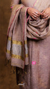 Person wearing a brown saree with gold stripes on a dark background