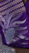 Close-up of a purple fabric with intricate silver embroidery on a brown background