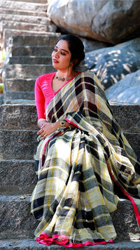 Woman sitting on stone steps wearing a black and yellow saree with a pink blouse.