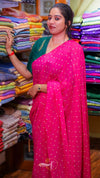 Woman in a pink saree standing in front of a colorful fabric display.