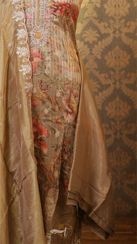 Close-up of a luxurious fabric with intricate patterns and embroidery on a textured wall background.