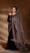 Woman wearing a black saree with a brown and white patterned shawl against a brown background