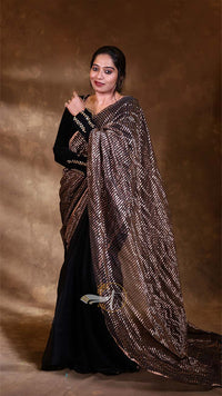 Woman wearing a black saree with a brown and white patterned shawl against a brown background
