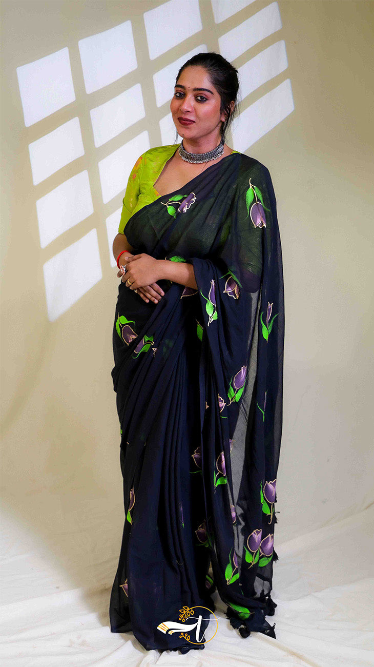 Woman wearing a black saree with floral patterns in a well-lit room.