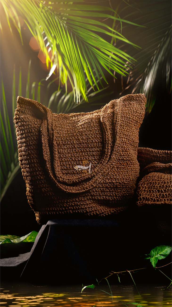 Brown crochet bag with a small logo on a dark background with green leaves