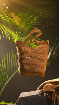 Brown woven bag with a small logo on a dark background with green leaves
