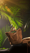 Brown woven bag on a dark surface with green leaves in the background