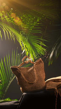 Brown woven bag on a dark surface with green leaves in the background
