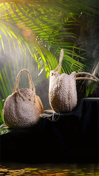Two woven bags on a dark surface with green foliage in the background