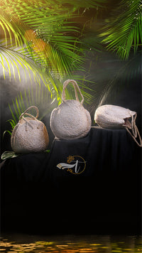 Three woven bags on a black surface with palm leaves in the background